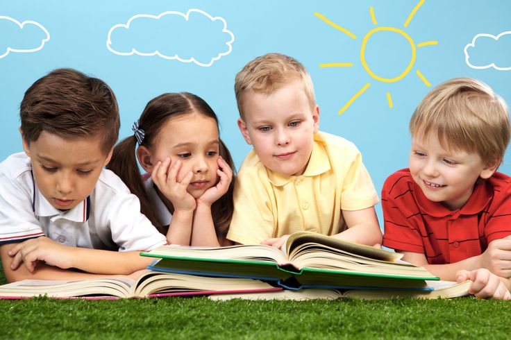 Group of happy children lying on a green grass and reading books